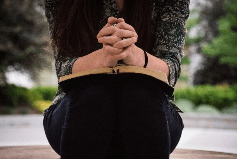 Picture of woman sitting and leaning forward with open Bible on her lap for post Bible journaling tips for beginners