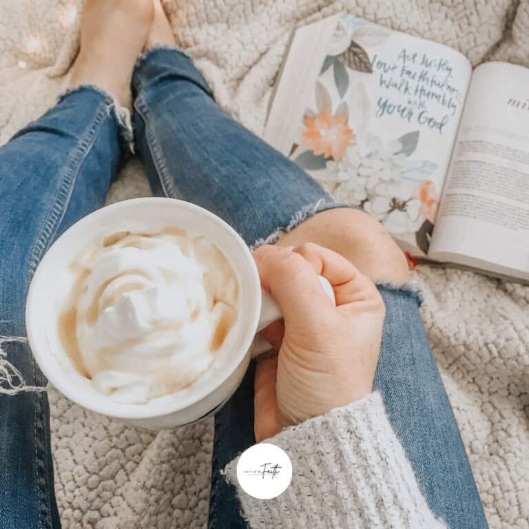 a person holding a coffee on a bed next to an open Bible