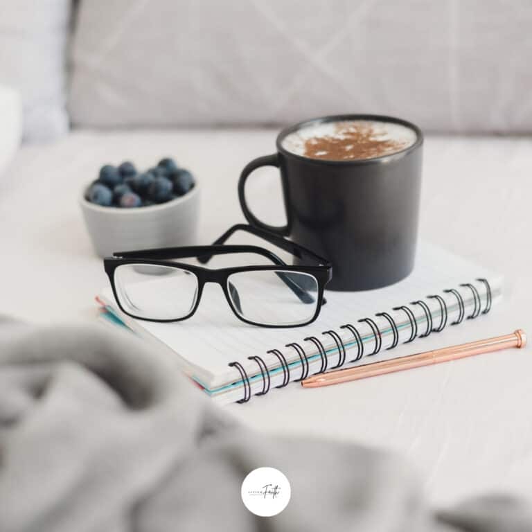 a notebook with glasses on top and a cup of coffee and bowl of blueberries