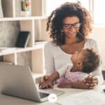 a mom holding a baby in front of a table with a laptop