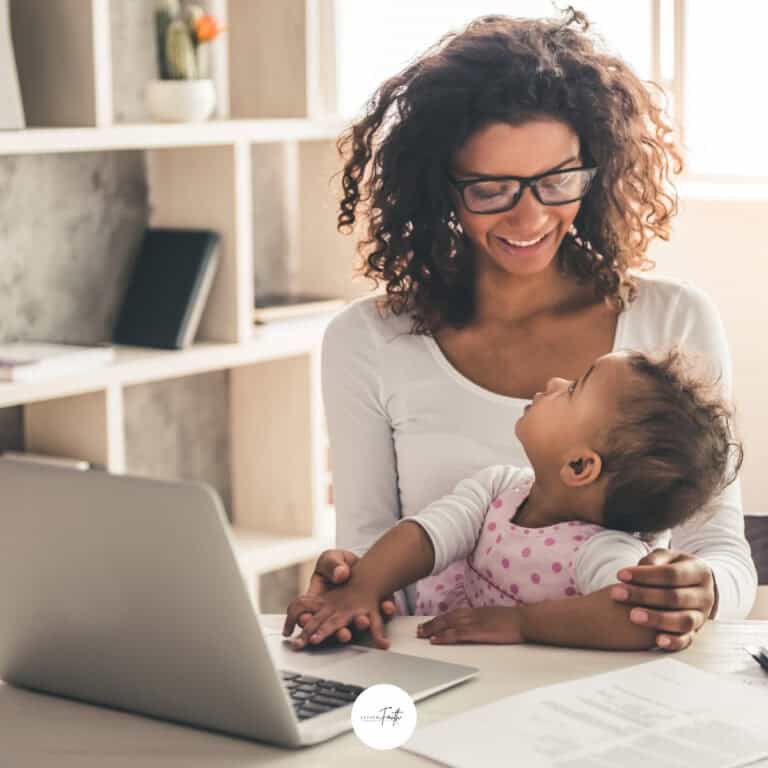 a mom holding a baby in front of a table with a laptop