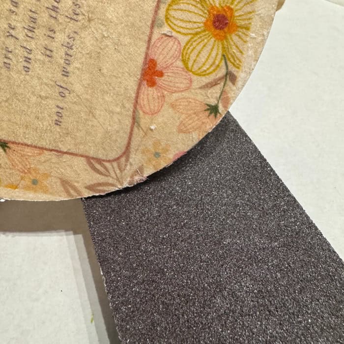 sanding block removing excess tissue paper from edges of wood circle for project using Christian Craft Paper
