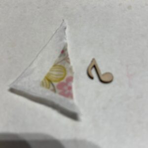torn corner of leftover tissue paper with small wooden musical notie